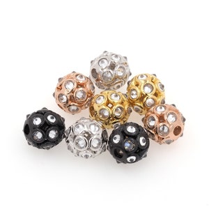 May include: A group of eight round beads with a variety of finishes, including silver, gold, black, and rose gold. Each bead is covered in small, clear rhinestones.