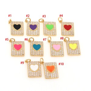Könnte beinhalten: Zehn goldfarbene Charms mit quadratischer Form und einem Herzdesign in der Mitte. Die Herzen sind mit verschiedenen Farben gefüllt: Schwarz, Lila, Grün, Rot, Rosa, Türkis, Hellrosa, Gelb, Weiß und Orange. Jeder Charm ist mit klaren Strasssteinen verziert.