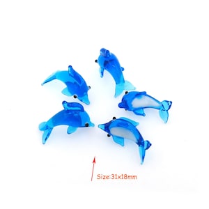 Peut inclure: Cinq figurines de dauphins en verre bleu avec des ventres blancs. Les dauphins sont disposés en cercle sur un fond blanc. Taille : 31x18mm.