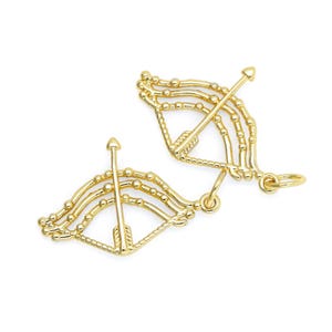 Può includere: Due ciondoli dorati a forma di arco e freccia con un design a perline. I ciondoli hanno un anello nella parte superiore per essere attaccati a una collana o un braccialetto.