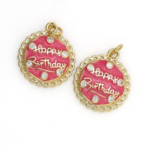 May include: Two gold-tone charms with a pink enamel finish and clear rhinestones. Each charm features the words "Happy Birthday" in a cursive script.