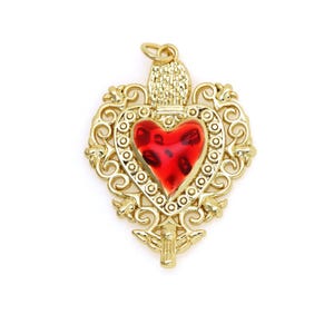 May include: A gold-tone pendant featuring a red glass heart with intricate filigree details. The heart is surrounded by a decorative border and the pendant has a loop at the top for hanging.