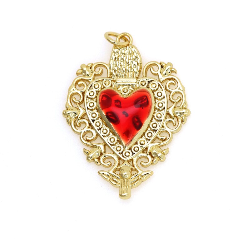 May include: A gold-tone pendant featuring a red glass heart with intricate filigree details. The heart is surrounded by a decorative border and the pendant has a loop at the top for hanging.
