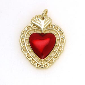 May include: A gold-tone pendant featuring a red heart with a flame design at the top. The heart is surrounded by a delicate filigree frame.