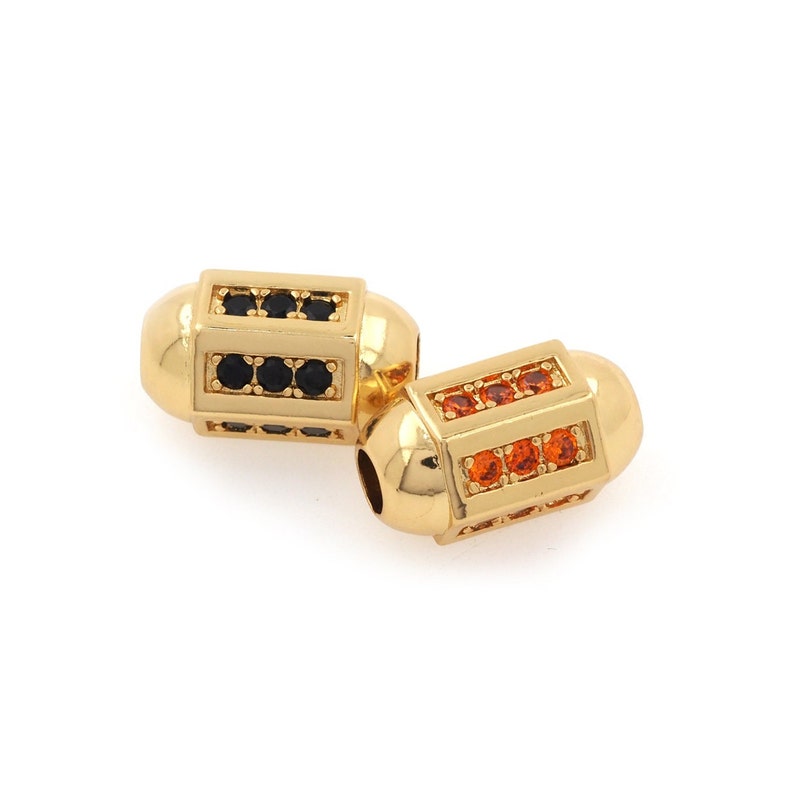 May include: Two gold-toned metal beads with a cylindrical shape. Each bead is decorated with a row of small, black or orange gemstones.
