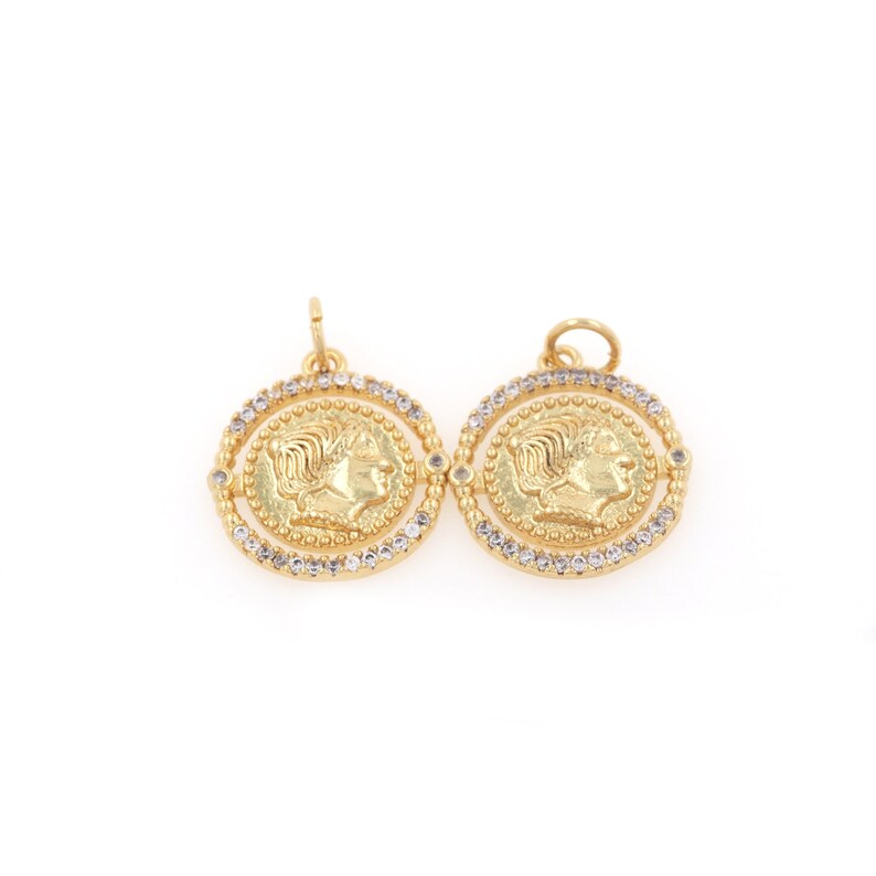 May include: Two gold-toned pendants with a raised profile of a woman's face on each. The pendants are surrounded by a circle of clear rhinestones.