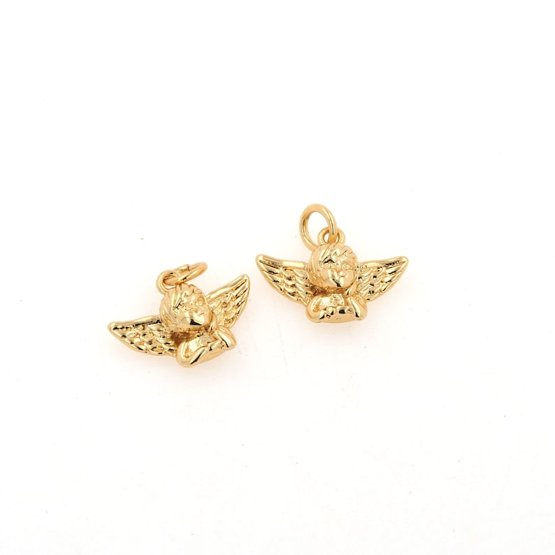 Op de afbeelding: Twee gouden engelbedels met vleugels en een slapend cherubijn gezicht. De bedels zijn perfect om een vleugje whimsy toe te voegen aan sieraden of knutselwerk.