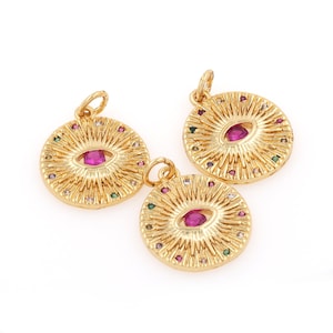 Könnte beinhalten: Drei goldfarbene Anhänger mit kreisförmigem Design. Jeder Anhänger zeigt ein pinkfarbenes Edelsteinauge, das von einem Ring aus kleineren bunten Edelsteinen umgeben ist.