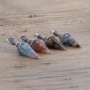 May include: Four crystal point pendants with silver accents. The pendants are made of clear resin with embedded crystals in shades of blue, brown, orange, and green.