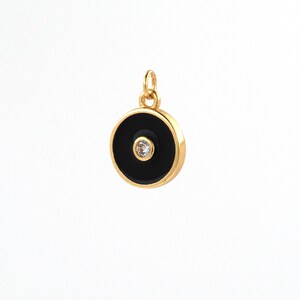 May include: Gold charm with a black enamel circle and a small clear rhinestone in the center.