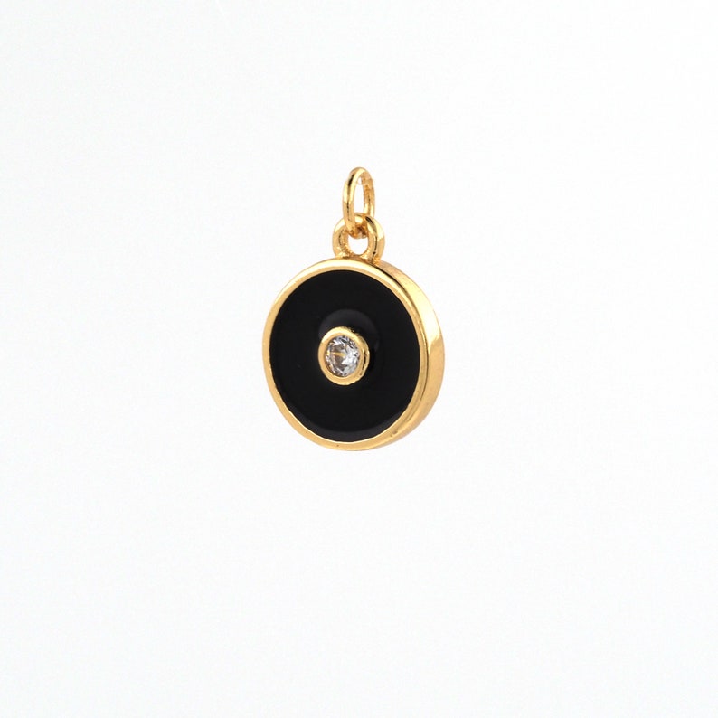 May include: Gold charm with a black enamel circle and a small clear rhinestone in the center.