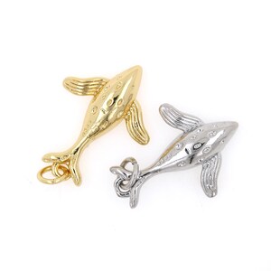 May include: Two whale charms, one gold and one silver, with a textured surface and a loop for attaching to a necklace or bracelet.