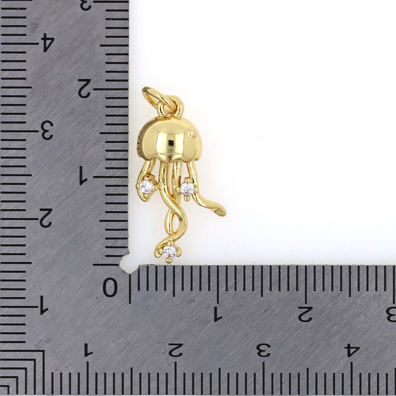 May include: Gold-tone charm in the shape of a jellyfish with clear cubic zirconia accents. The charm is approximately 1 inch in length.