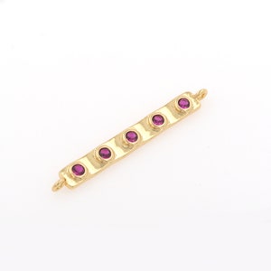 May include: Gold bar charm with five purple gemstones. The bar has a textured surface and a loop at one end.