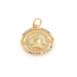 May include: Gold pendant with a detailed profile of a woman's face on a round coin surrounded by a circle of clear rhinestones.