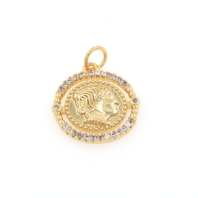 May include: Gold pendant with a detailed profile of a woman's face on a round coin surrounded by a circle of clear rhinestones.