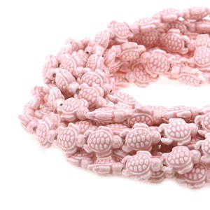 May include: A strand of pink ceramic turtle beads. The beads are all the same size and shape, and they are strung together on a clear thread.