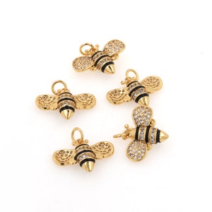May include: Five gold bee charms with black and white enamel details and clear crystal accents. The bee charms are perfect for jewelry making or adding a touch of whimsy to crafts.