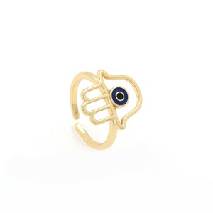 Pu&ograve; includere: Anello in oro con un design a mano di hamsa e un occhio blu malvagio al centro.