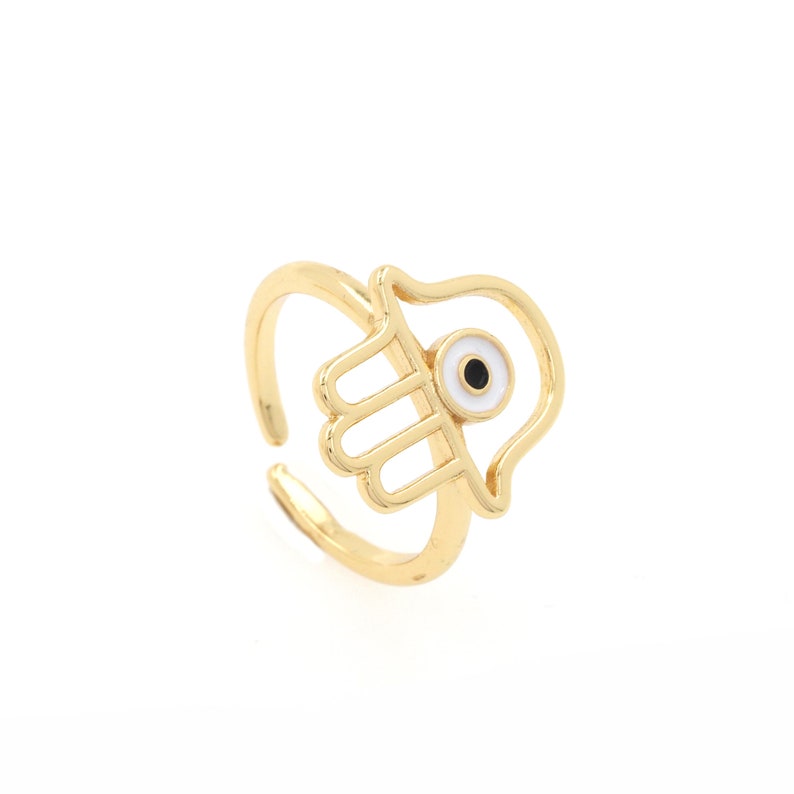 Pu&ograve; includere: Anello in oro con un design a mano di hamsa e un ciondolo di occhio turco bianco.