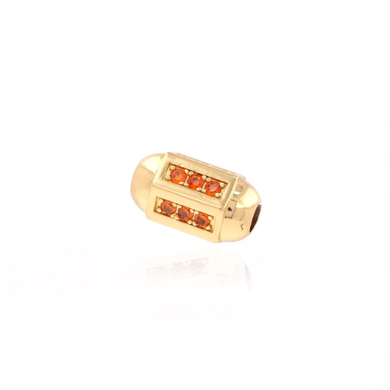 May include: Gold-toned bead with a rectangular design featuring a row of orange gemstones on each side.