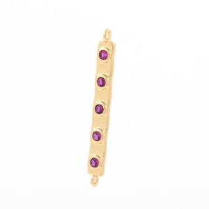 May include: Gold bar connector with five purple gemstones. The connector has two loops at the top and bottom.