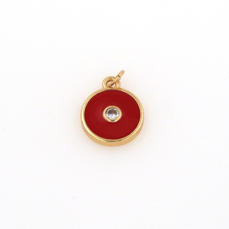 May include: Gold charm with a red enamel circle and a small clear rhinestone in the center.