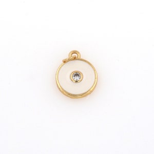 May include: Gold charm with a white enamel circle and a small clear rhinestone in the center.