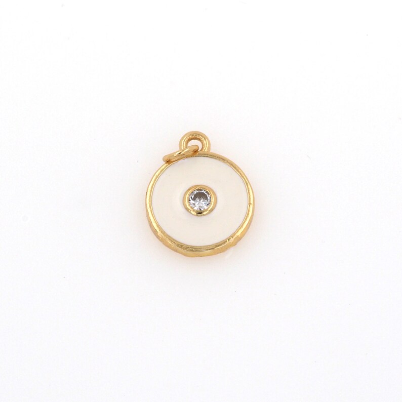 May include: Gold charm with a white enamel circle and a small clear rhinestone in the center.