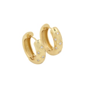 May include: Gold hoop earrings with a starburst design and clear cubic zirconia stones.