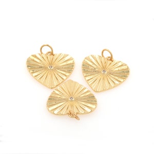 May include: Three gold heart-shaped charms with a sunburst design and a small clear rhinestone in the center. The bottom charm has a loop for attaching to a necklace or bracelet.