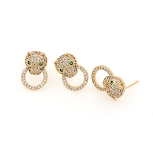 May include: Gold tone earrings with a panther head design and clear and green cubic zirconia stones.