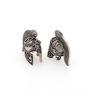 May include: Two silver-toned, detailed, miniature Roman helmet charms. Each helmet has a plume on the top and intricate designs on the sides.