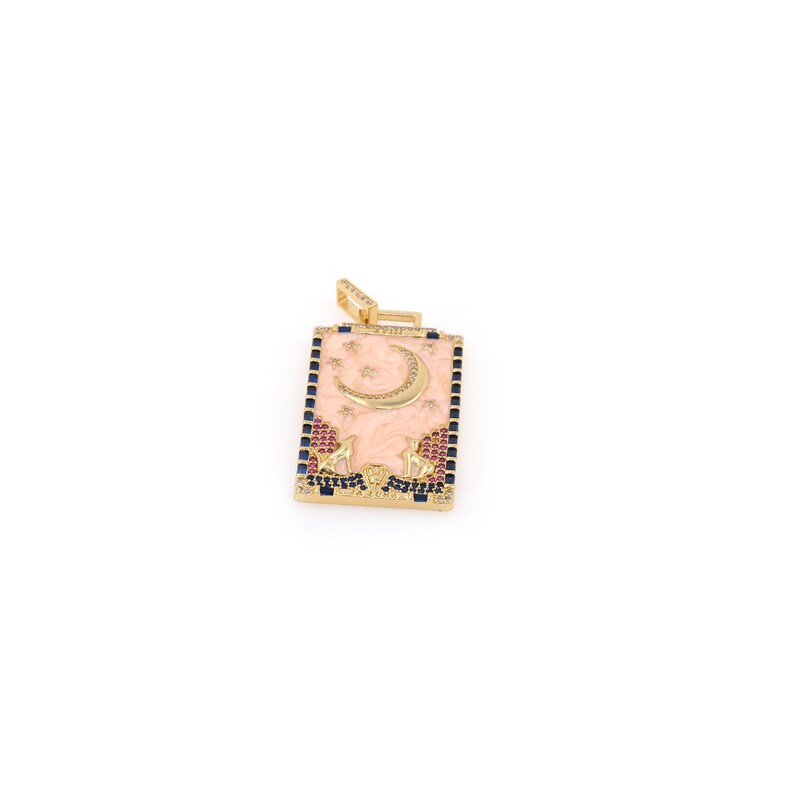May include: Gold pendant with a pink enamel rectangle featuring a crescent moon and stars. The pendant is decorated with blue and red gemstones.
