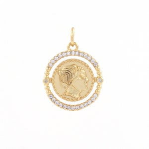 May include: Gold pendant with a profile of a woman's face on a round coin surrounded by a circle of clear rhinestones.