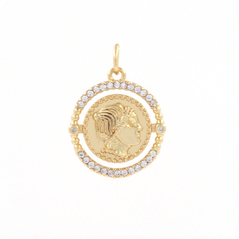 May include: Gold pendant with a profile of a woman's face on a round coin surrounded by a circle of clear rhinestones.