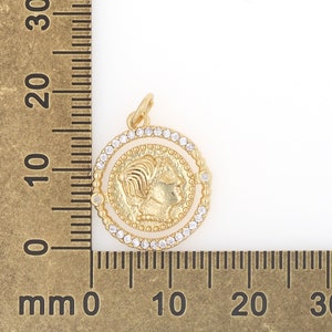 May include: Gold-toned pendant featuring a profile of a woman's face surrounded by a circle of clear rhinestones. The pendant is approximately 2 cm in diameter.
