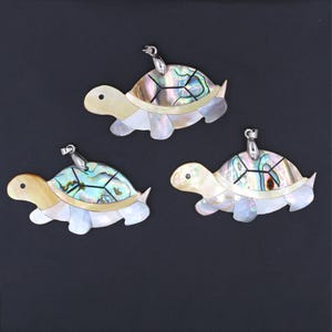 May include: Three iridescent abalone shell turtle pendants with silver tone bail. The turtles are a light beige color with a multi-colored abalone shell design.