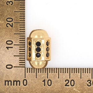 May include: A gold-colored bead with black accents. The bead is approximately 1 cm in diameter and has a geometric design.