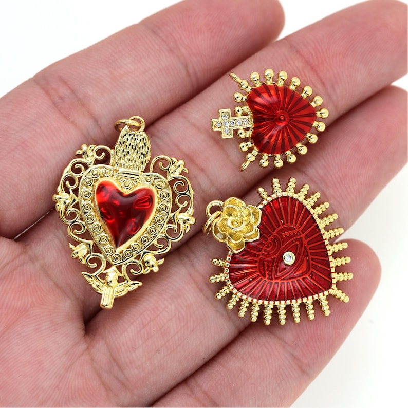 May include: Three gold-tone heart-shaped pendants with red enamel and rhinestones. The pendants feature intricate designs and are perfect for jewelry making.