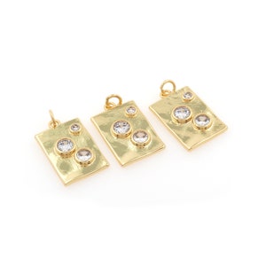 Puede incluir: Tres colgantes de oro con detalles de cristal transparente. Cada colgante es rectangular con esquinas redondeadas y presenta una textura martillada.