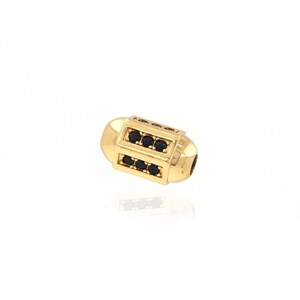 May include: Gold-toned bead with black cubic zirconia stones. The bead is cylindrical and has a smooth, polished finish.
