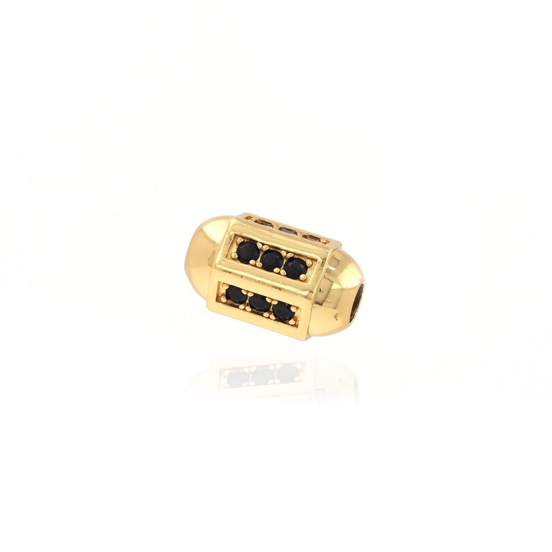 May include: Gold-toned bead with black cubic zirconia stones. The bead is cylindrical and has a smooth, polished finish.