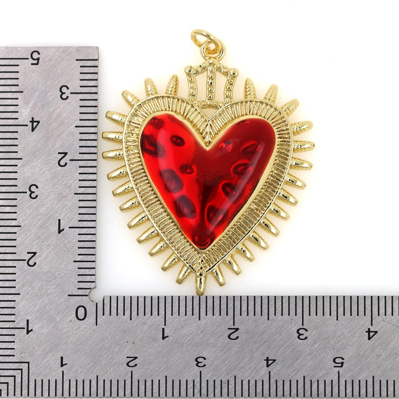 May include: Gold-tone pendant featuring a red heart with a crown on top. The heart is surrounded by a gold-tone halo with spikes. The pendant is approximately 2 inches in diameter.