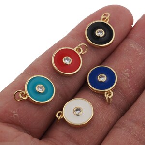 May include: Five gold-tone charms with a round, flat design. Each charm has a different colored enamel center with a clear rhinestone in the center. The colors are black, red, turquoise, blue, and white.