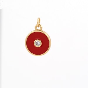 May include: A gold charm with a red enamel circle and a small clear rhinestone in the center.