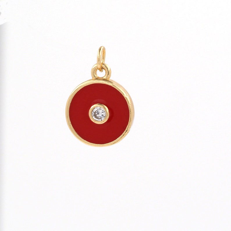 May include: A gold charm with a red enamel circle and a small clear rhinestone in the center.