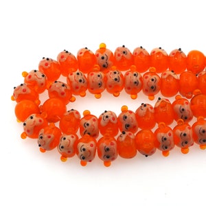 May include: A strand of orange glass beads with a smiling face design. The beads are round and have a glossy finish.