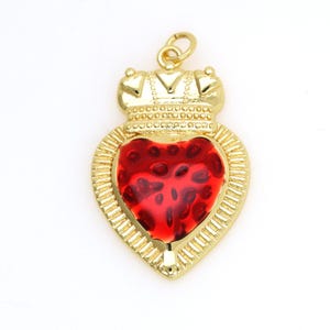 May include: A gold-tone pendant charm in the shape of a heart with a red enamel center. The heart is topped with a small crown.