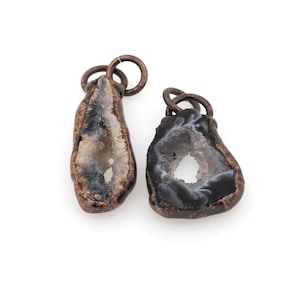 May include: Two agate geode pendants with copper wire wrapped around the edges. The geodes are both open and have a white interior with a black and white pattern.
